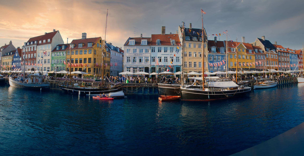 Nyhavn harbour in Copenhagen at sunset, with colourful waterfront houses and boats reflected in dark blue water